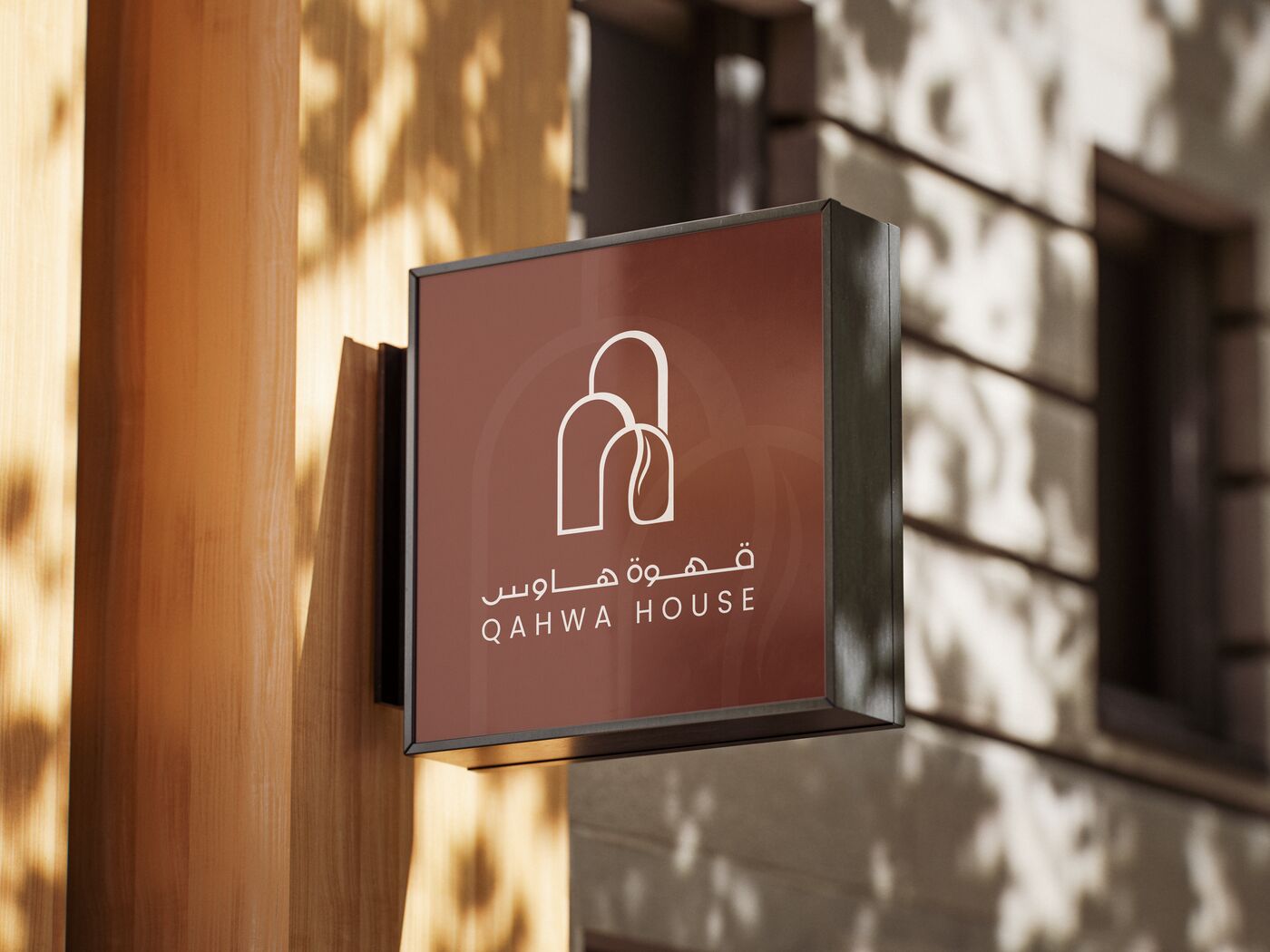 The Qahwa House sign, brown with the cream logo, on a sunlit wall